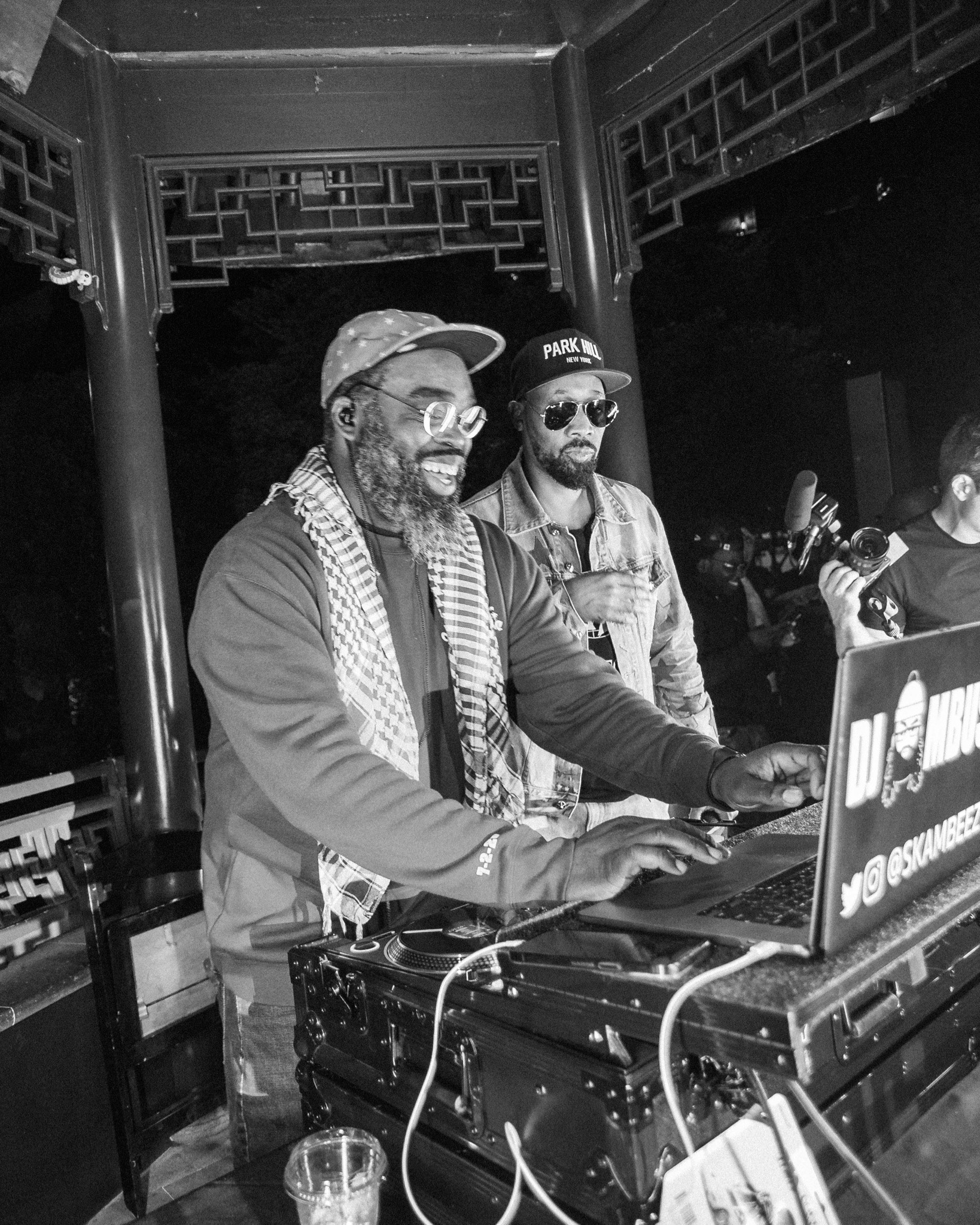 Black and white photograph of DJ Ambush smiling behind a laptop, standing next to RZA.