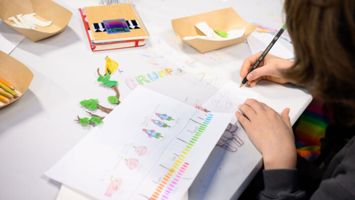 Photo of a kid drawing at a table of paper, colored pencils, and art supplies.