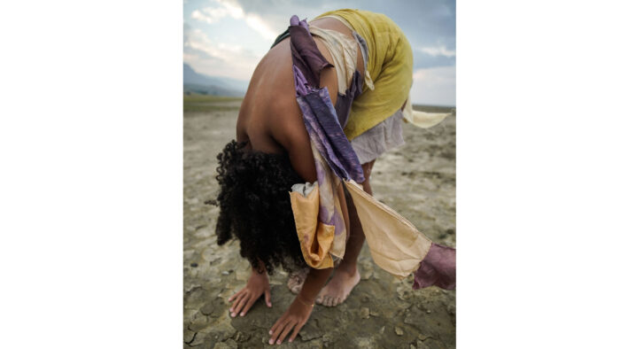 Photo of a woman on a beach bending over in a forward fold.
