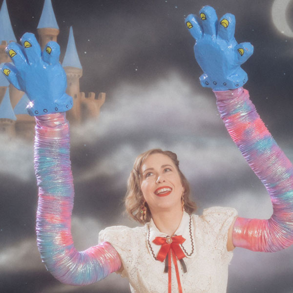 Photo of a person with clouds behind them and large colorful fake arms and hands in the air
