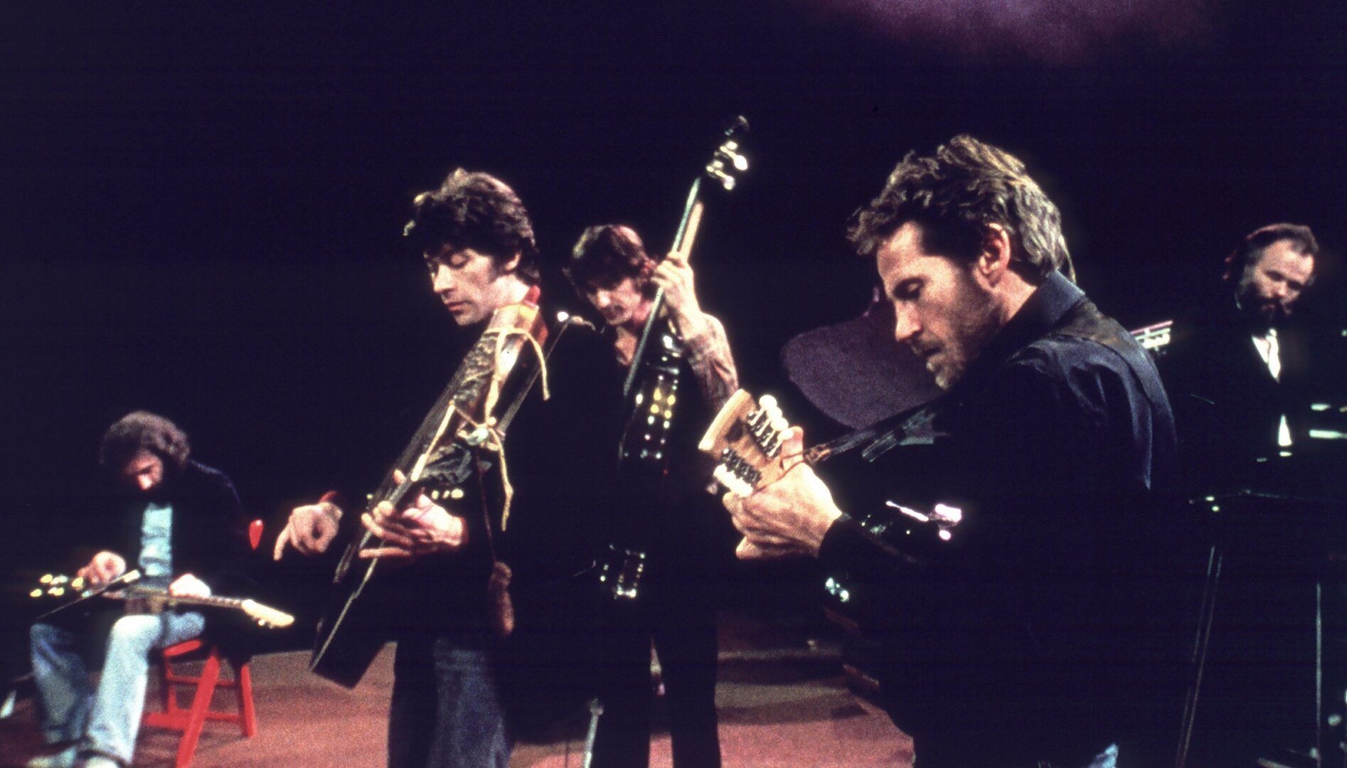 Film still of a group of men playing instruments on a stage.
