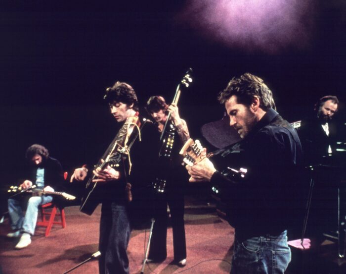 Film still of a group of men playing instruments on a stage.