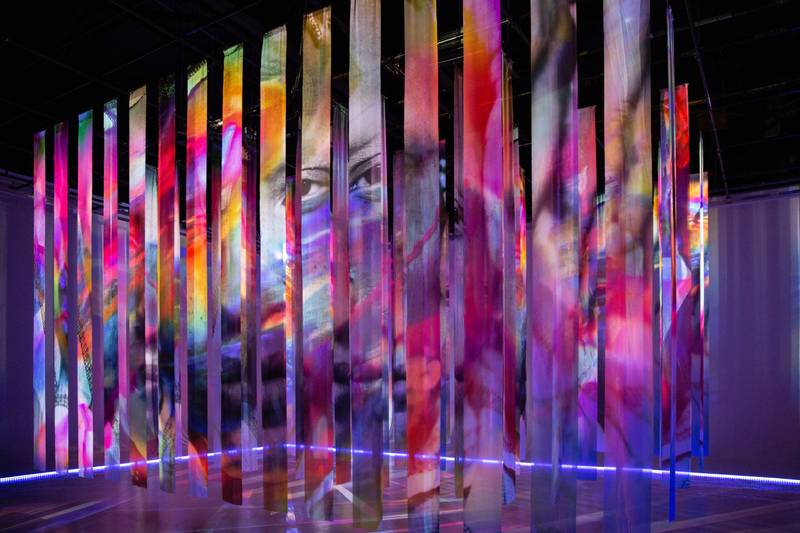 A multi-colored artwork with video projections of a face and patterns on strips of fabric.