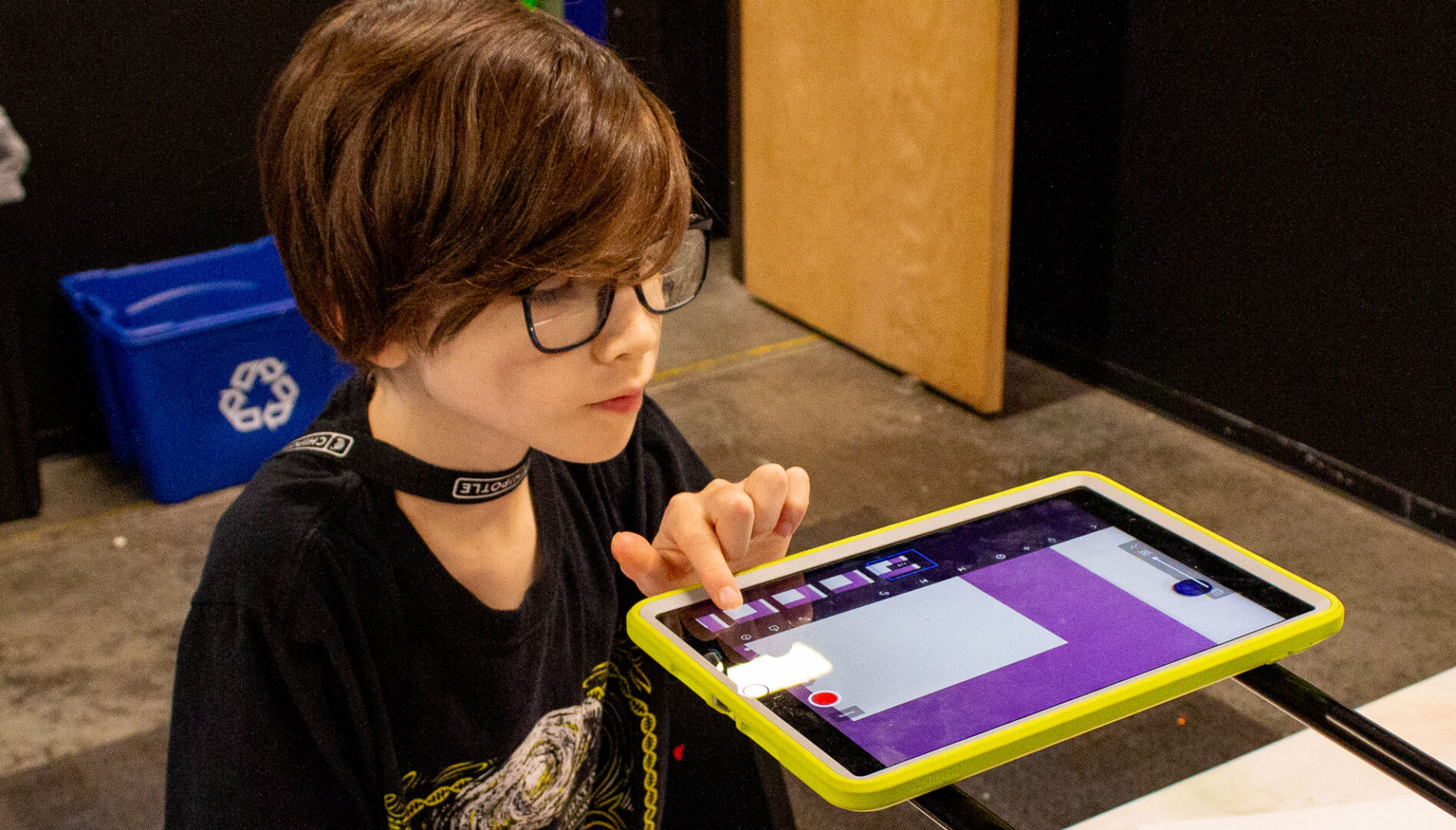 A child with short hair and eyeglasses making art on an iPad.