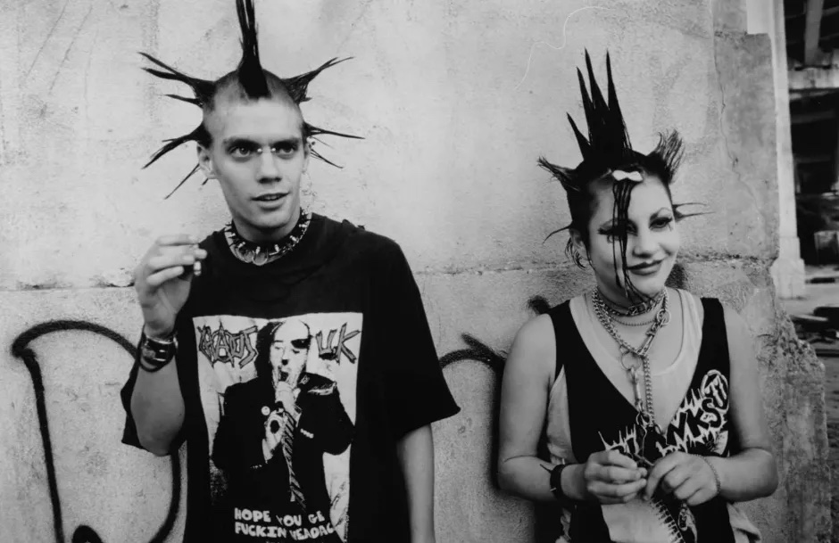Black and white film still of a two punk rockers with spiky hair against a graffitied wall.