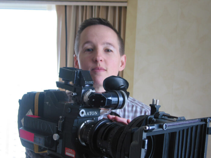 A woman with short hair standing behind a movie camera.