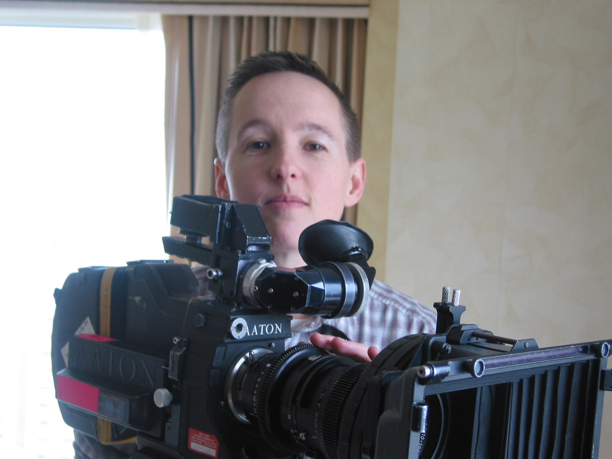 A woman with short hair standing behind a movie camera.