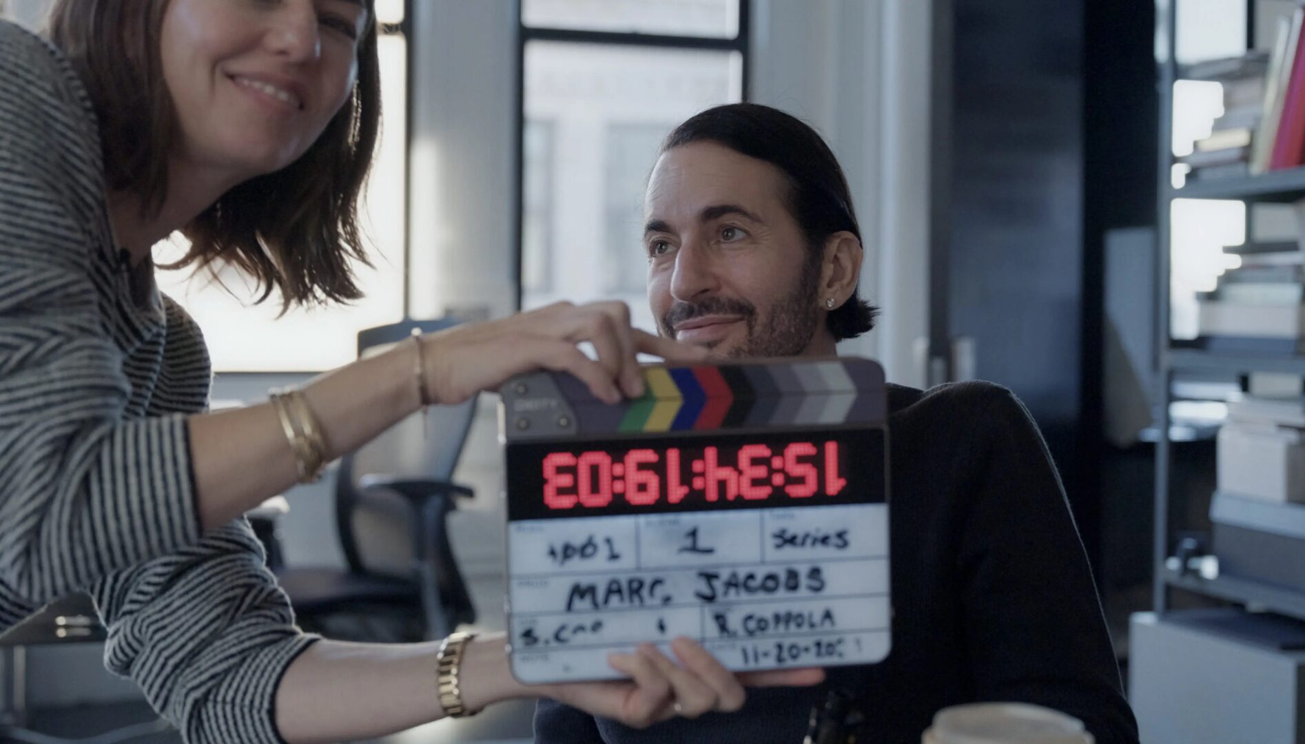 Sofia Coppola leaning in with a clapboard in front of Marc Jacobs who is looking lovingly at her.