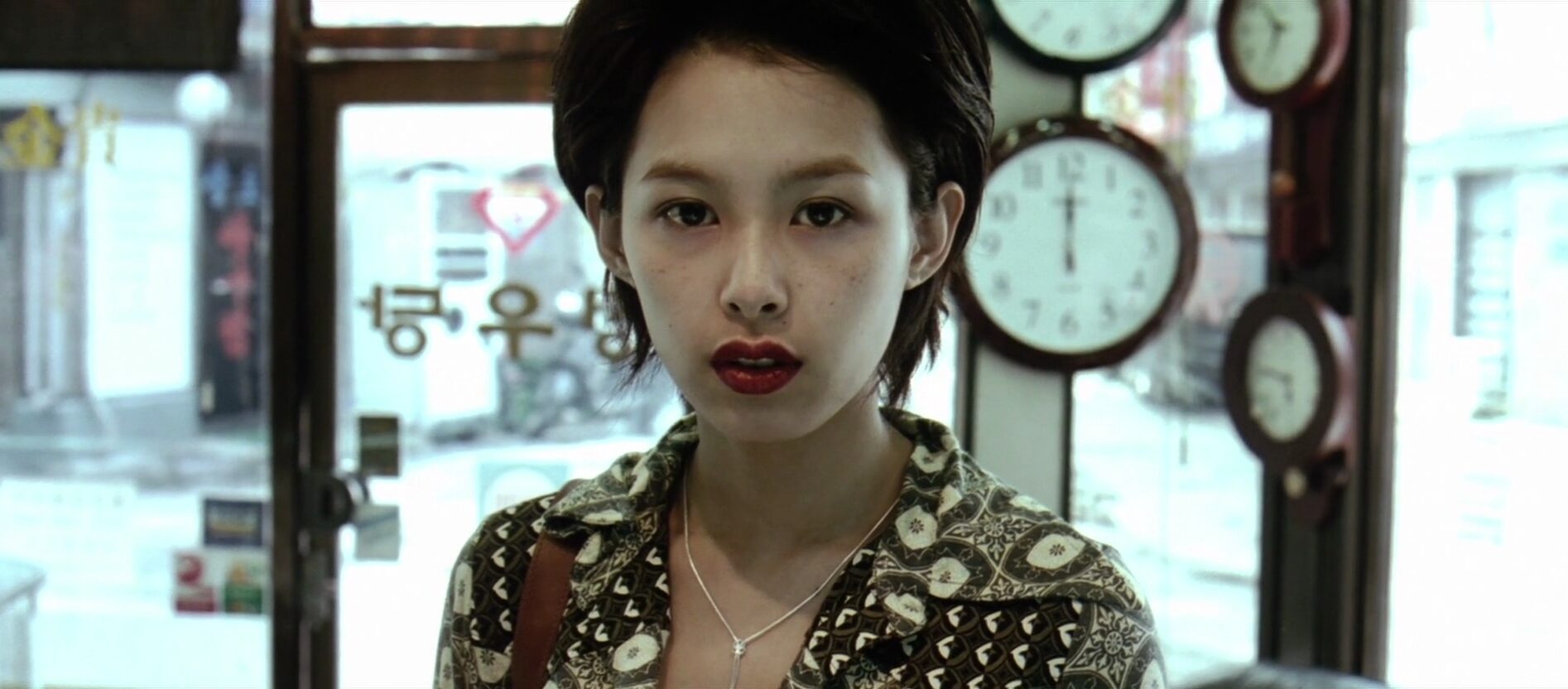 A woman with short hair standing in front of windows and a door with many clocks behind her.