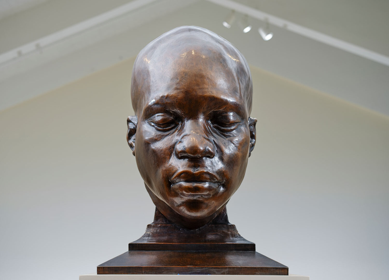 A bronze sculpture of a Black man's face and neck. His eyes are closed.