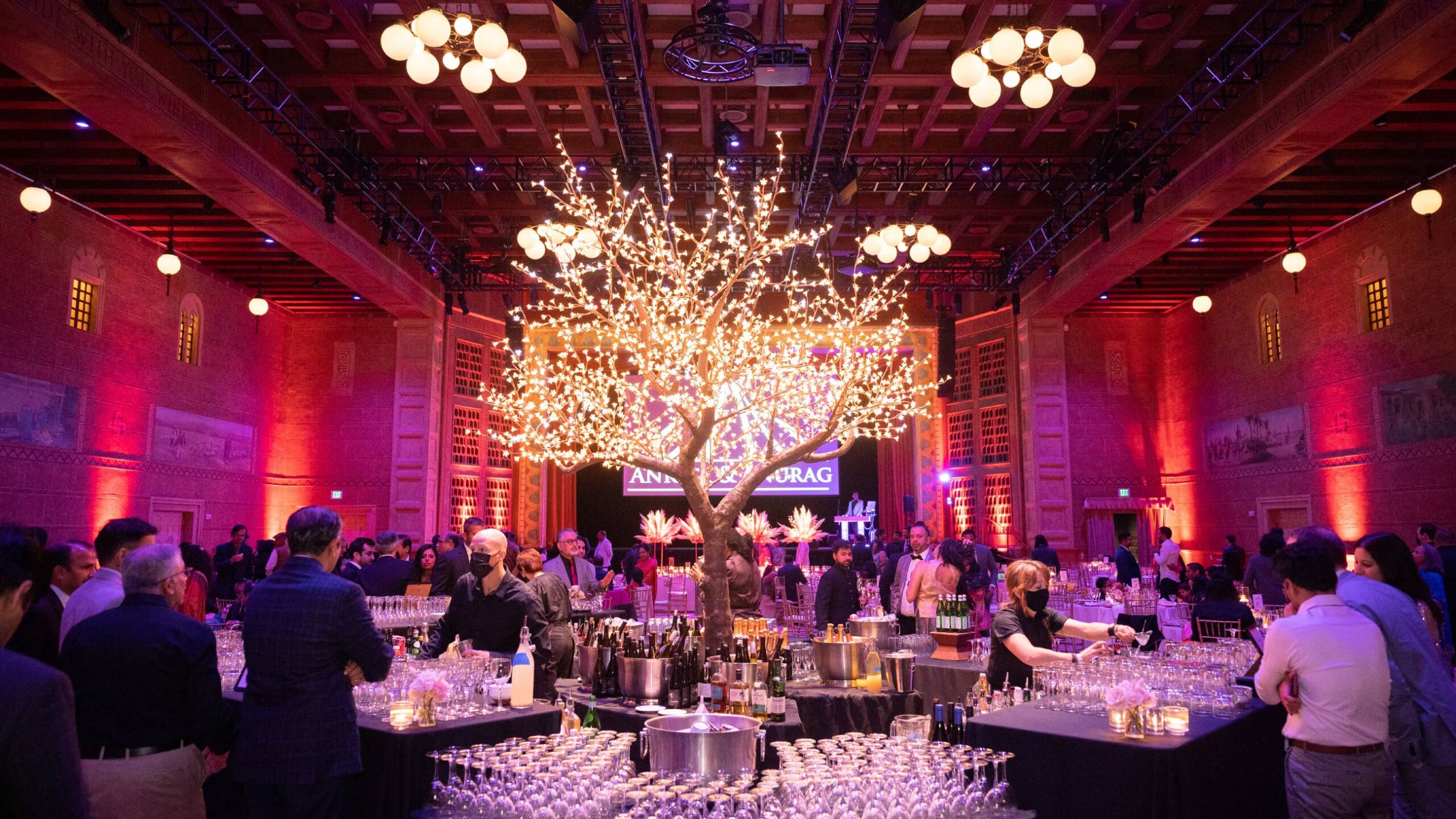 A ballroom with a large tree covered in lights, staffed with bartenders.