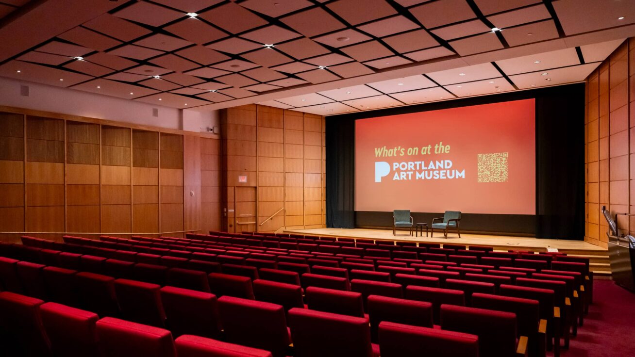 An auditorium with a movie screen, stage, and rows of seats.