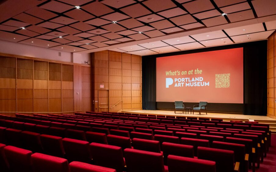 An auditorium with a movie screen, stage, and rows of seats.