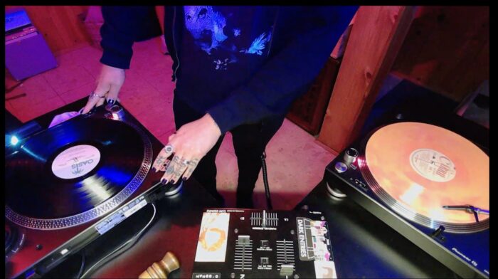 Photo of a DJ behind two turntables and a mixer.