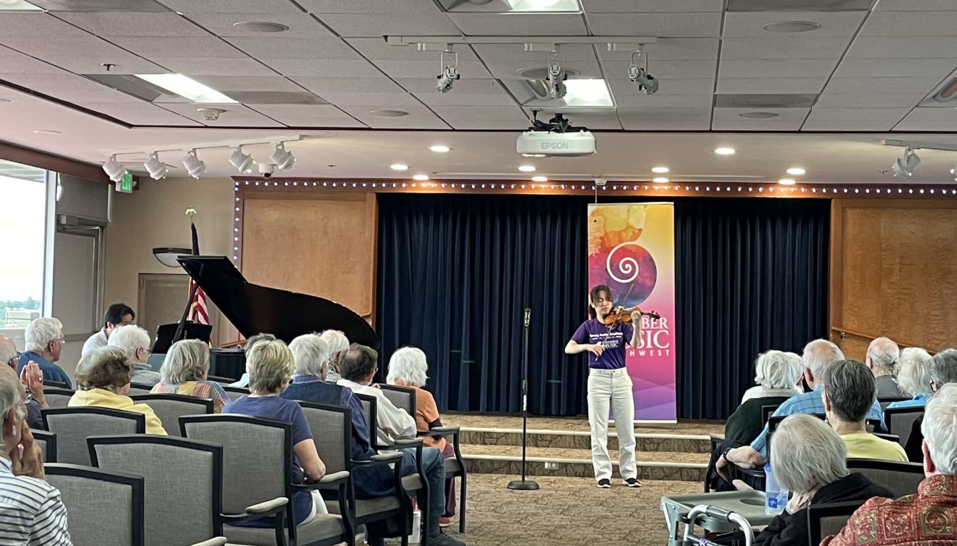 Photo of a young violin player playing to a room of seated people.