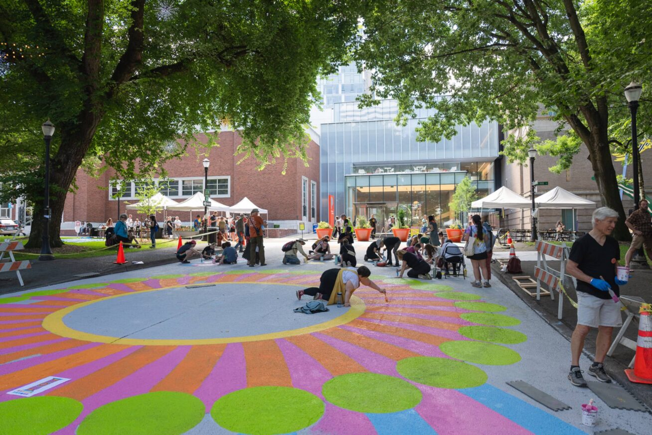 Several people installing a colorful mural on a walking path.