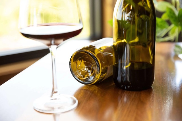 Photo of a glass of wine with two bottles on a table.