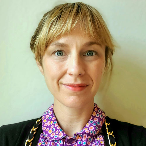 Photo of a woman with blonde hair, wearing a brightly colored collard shirt.