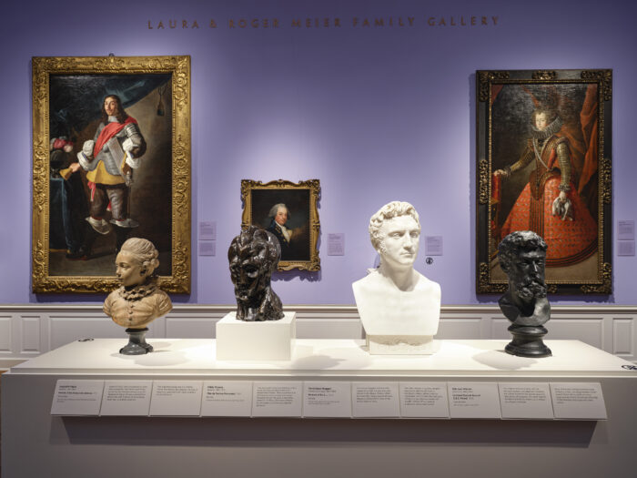 Photo of a gallery with purple walls, paintings on the walls and four bust sculptures in the foreground.