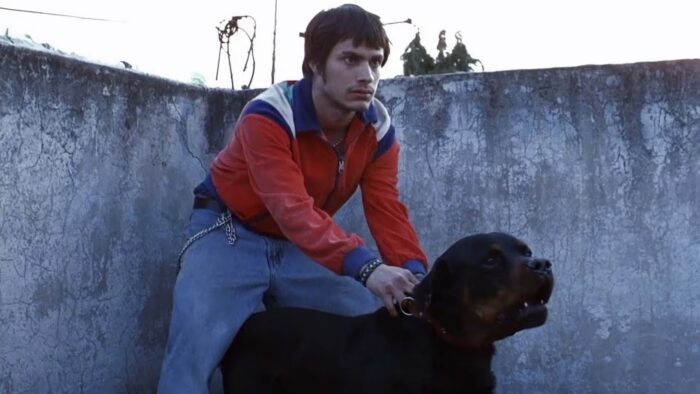 A young man in a red jacket holding onto the collar of a big dog.