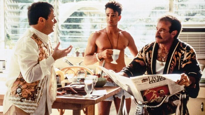 Film still of three men around a kitchen table. One is holding a coffee cup and one a newspaper.