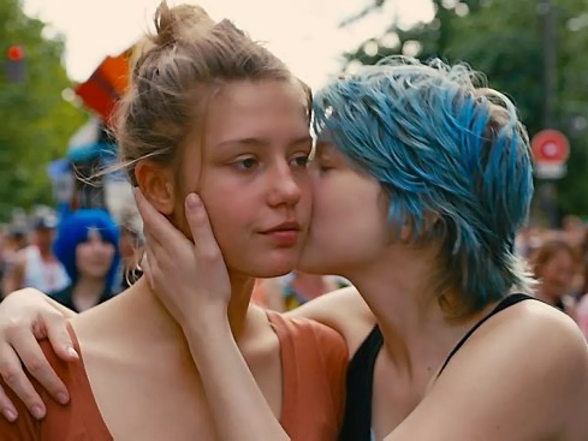A young woman with blue hair kissing another young woman's cheek.