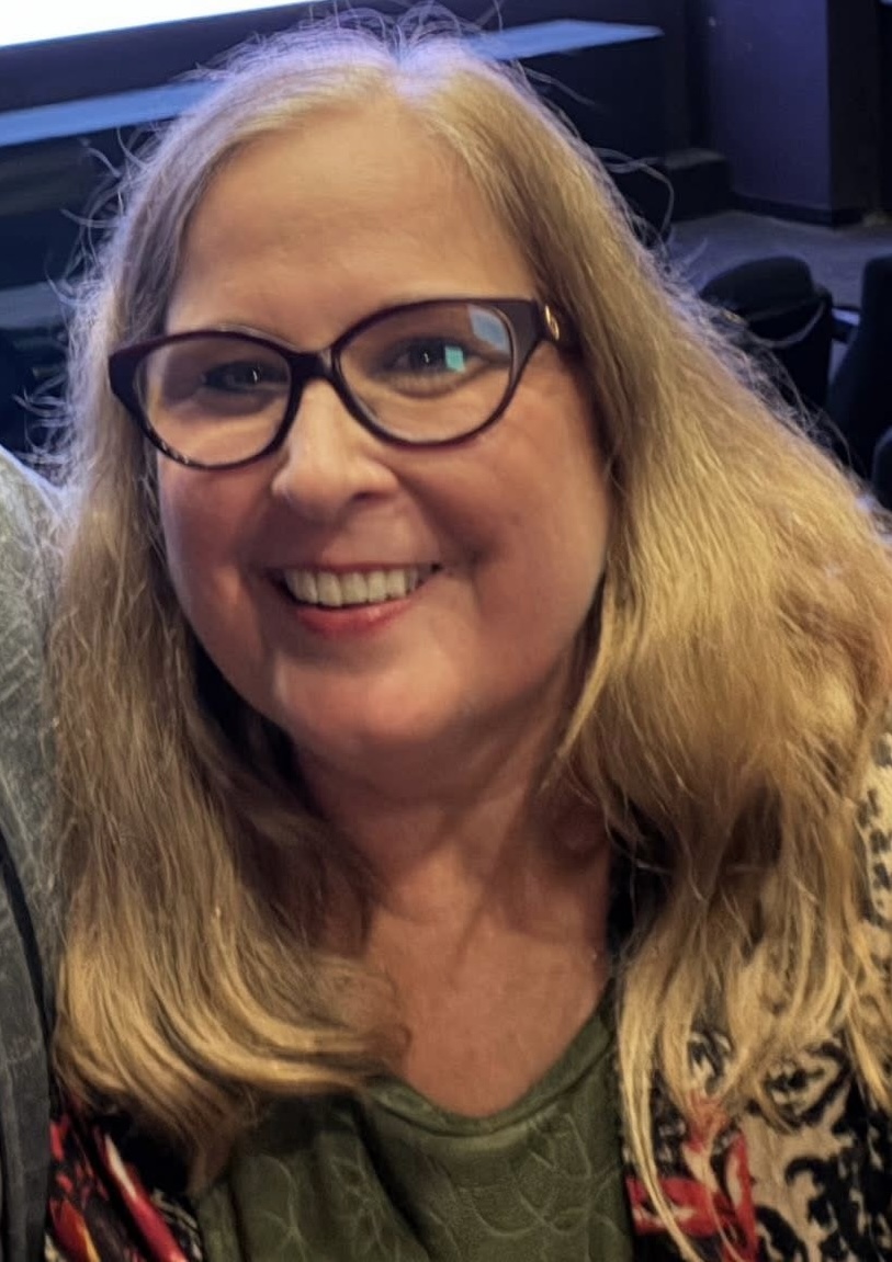 Photo of a smiling woman with long blonde hair, wearing eyeglasses.