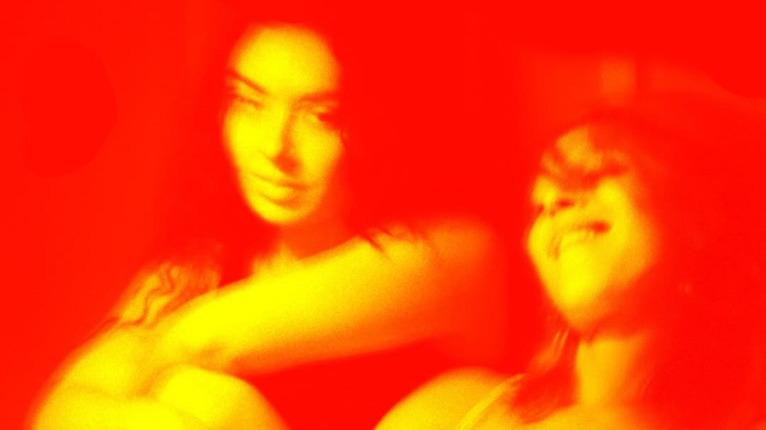 A red and yellow-orange tinted image of two young women.