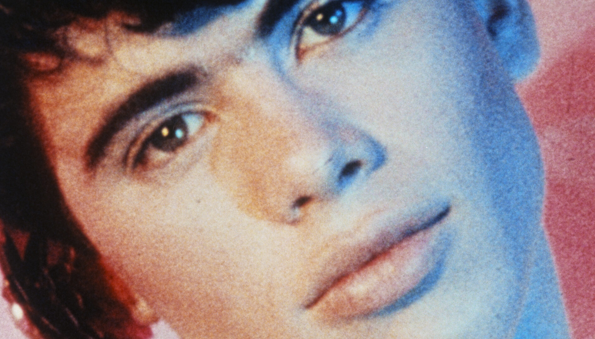 Close-up film still of a young man's face. He has brown hair and his head tilted to the side.