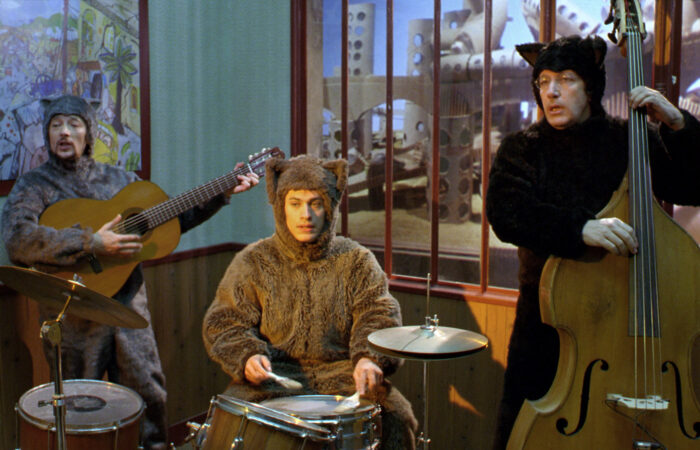 Three people in brown animal costumes playing instruments.
