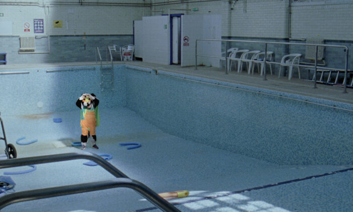 Film still of a person in a panda costume standing in an empty swimming pool.