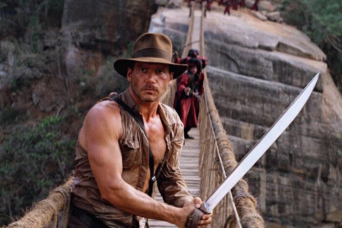 Film still of Indiana Jones on a rope bridge, holding a sword.
