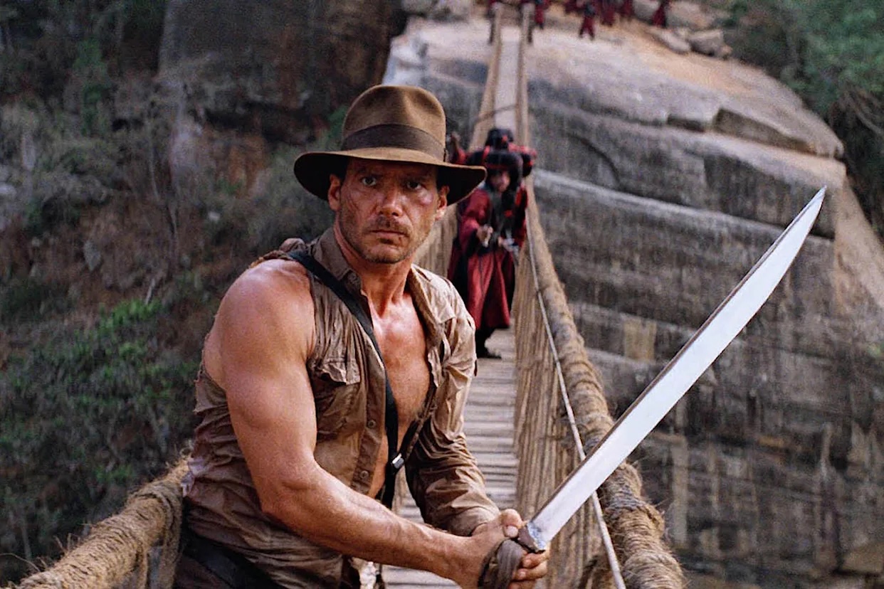 Film still of Indiana Jones on a rope bridge, holding a sword.