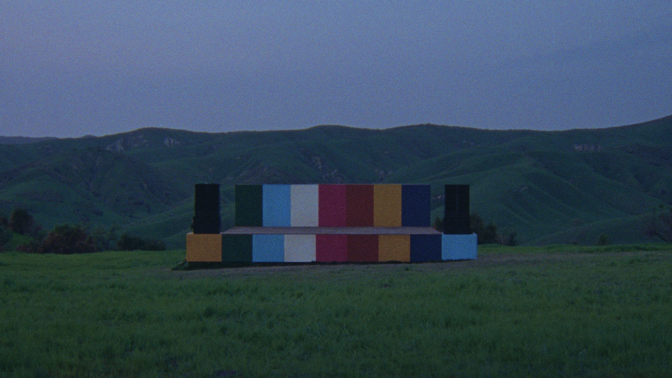 A dim photo of grass and hills with a stack of different colored boxes in the middle.
