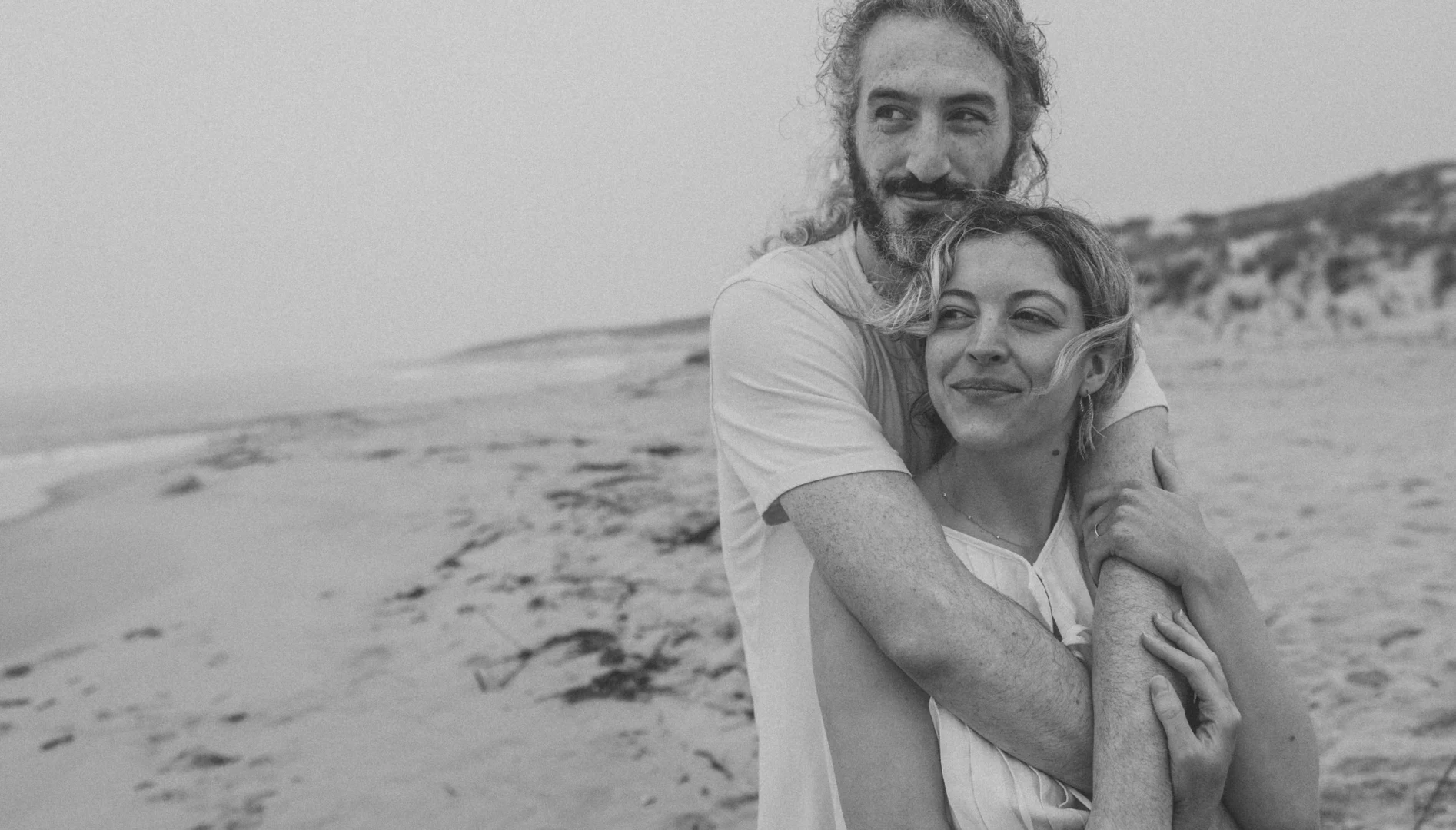 Black and white photo of a man and woman hugging on the beach.