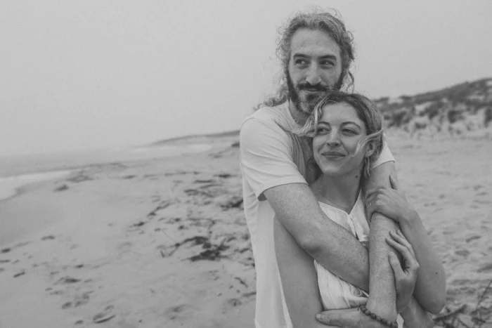 Black and white photo of a man and woman hugging on the beach.