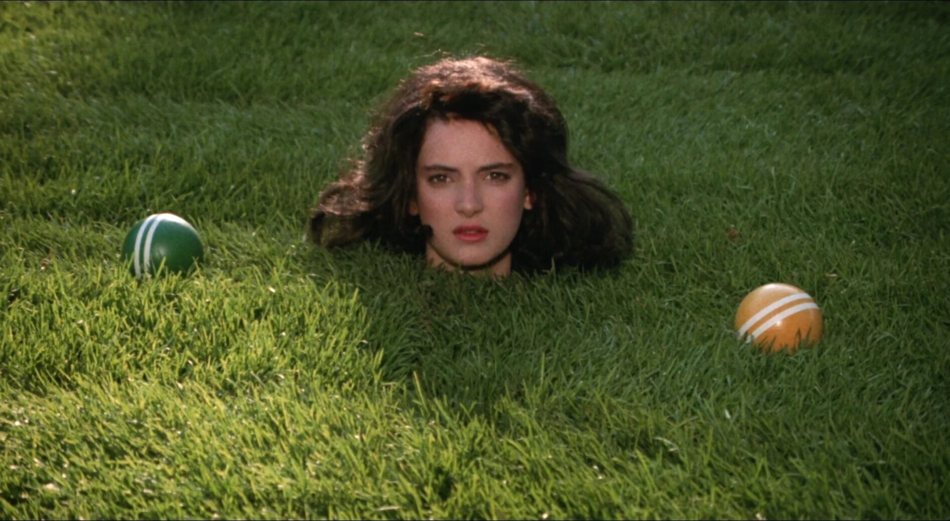 Photo of a woman's head popping out of the grass with two croquet balls next to her head.