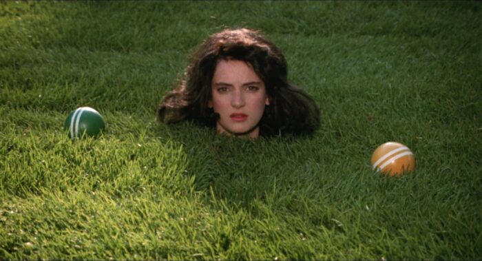 Photo of a woman's head popping out of the grass with two croquet balls next to her head.
