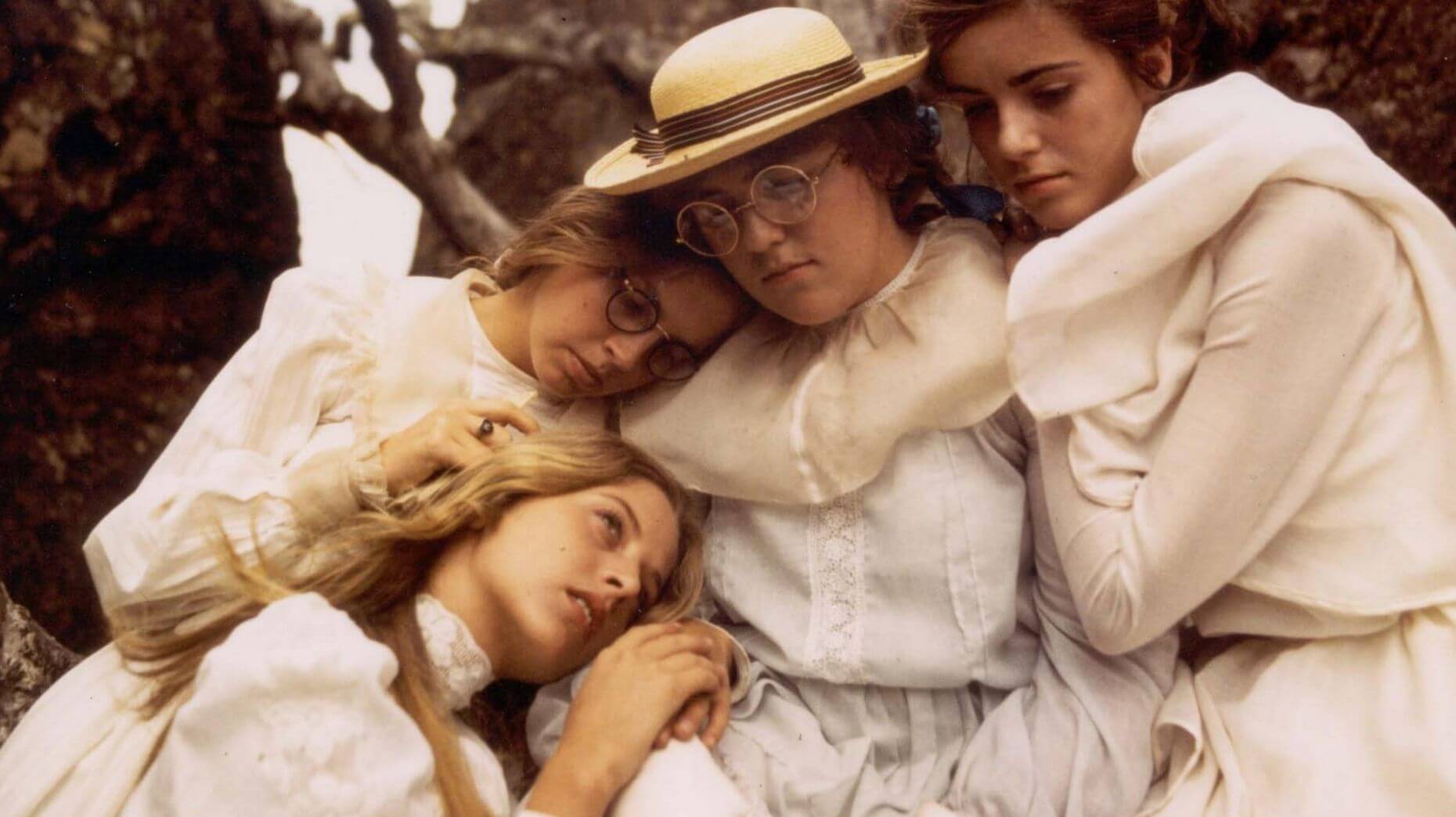 Photo of four young women in white dresses hugging each other.