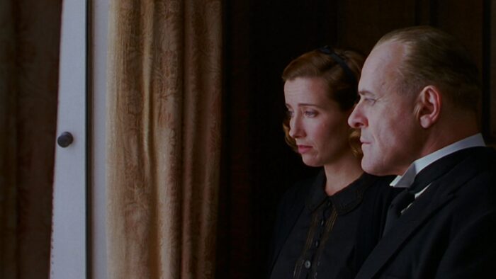 A man and a woman with serious faces looking out a window.