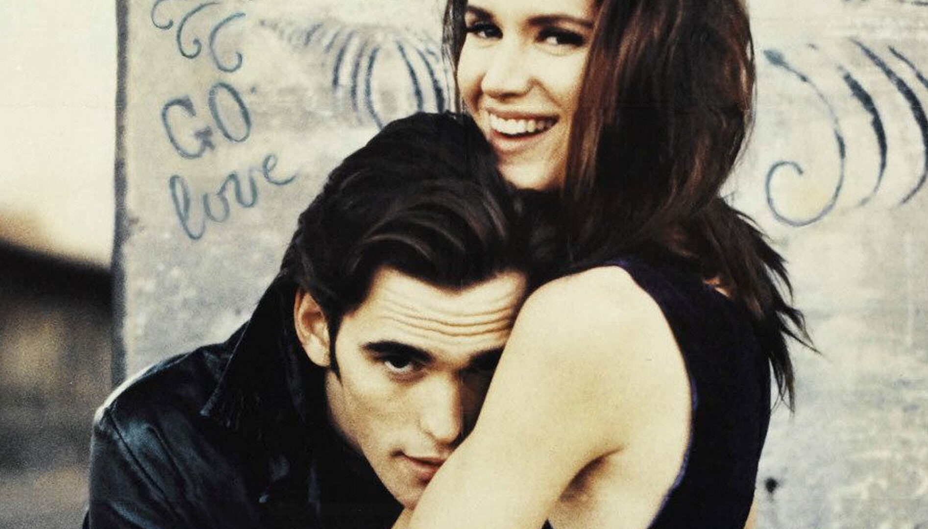 A man with dark brown hair hugging a smiling woman with long dark hair.