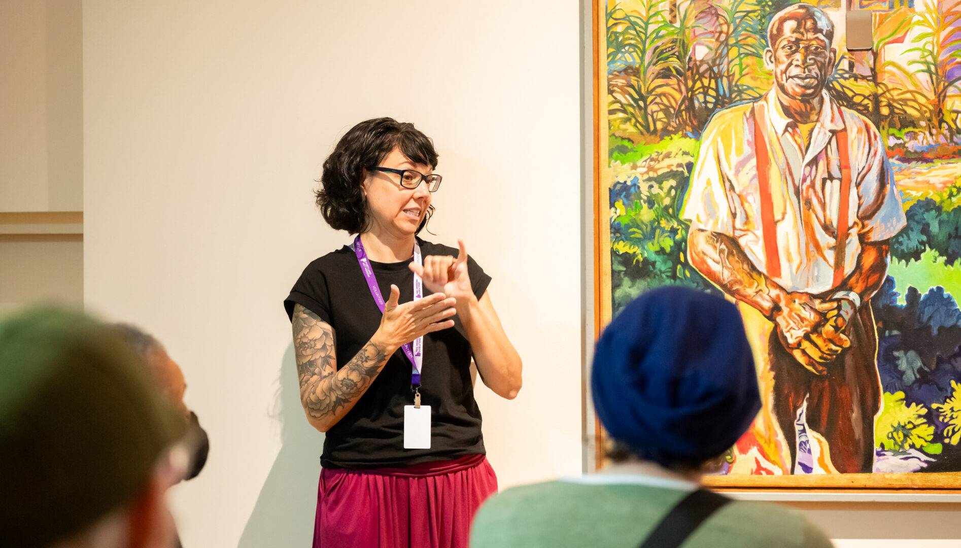 Woman doing sign language in front of a painting by Isaka Shamsud Din.