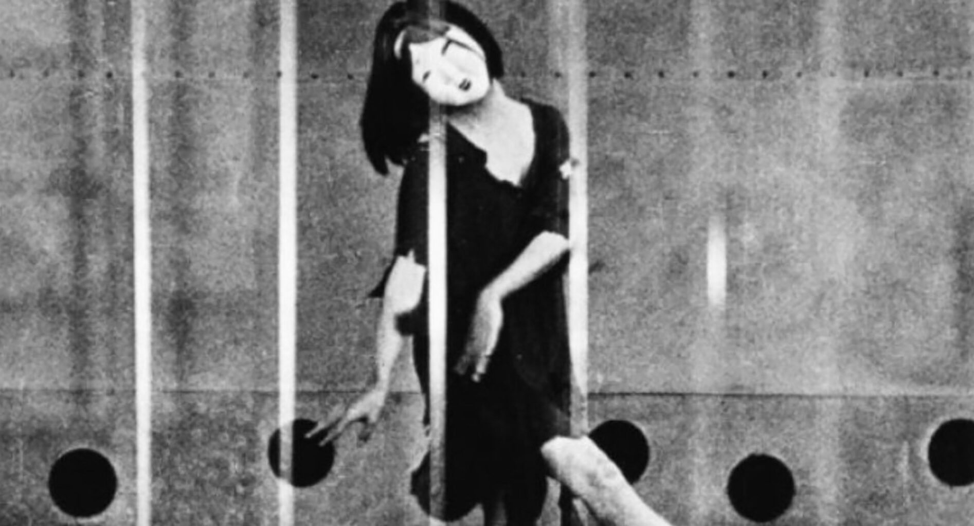Black and white film still of a person wearing a mask and dancing.