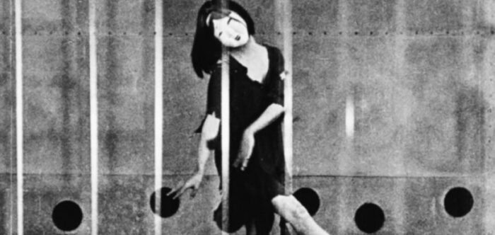 Black and white film still of a person wearing a mask and dancing.