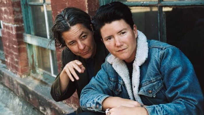 Film still of two women looking out a window against a brick building.