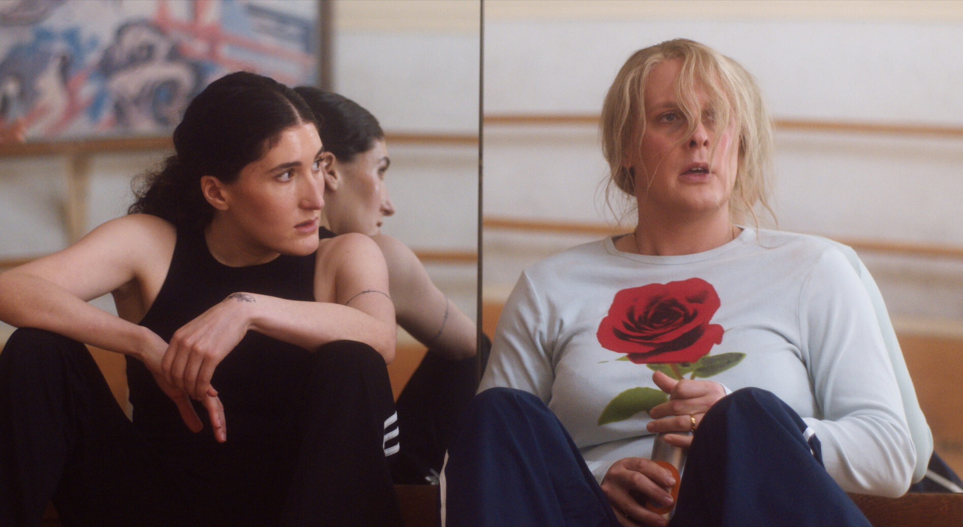 Film still of two people sitting on the ground against a mirror.