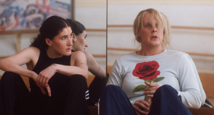 Film still of two people sitting on the ground against a mirror.