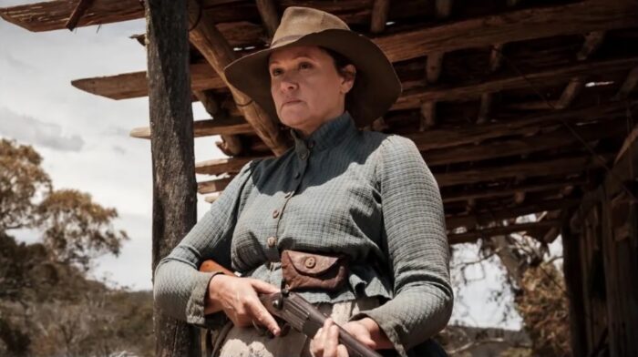 A woman wearing a hat and holding a rifle.