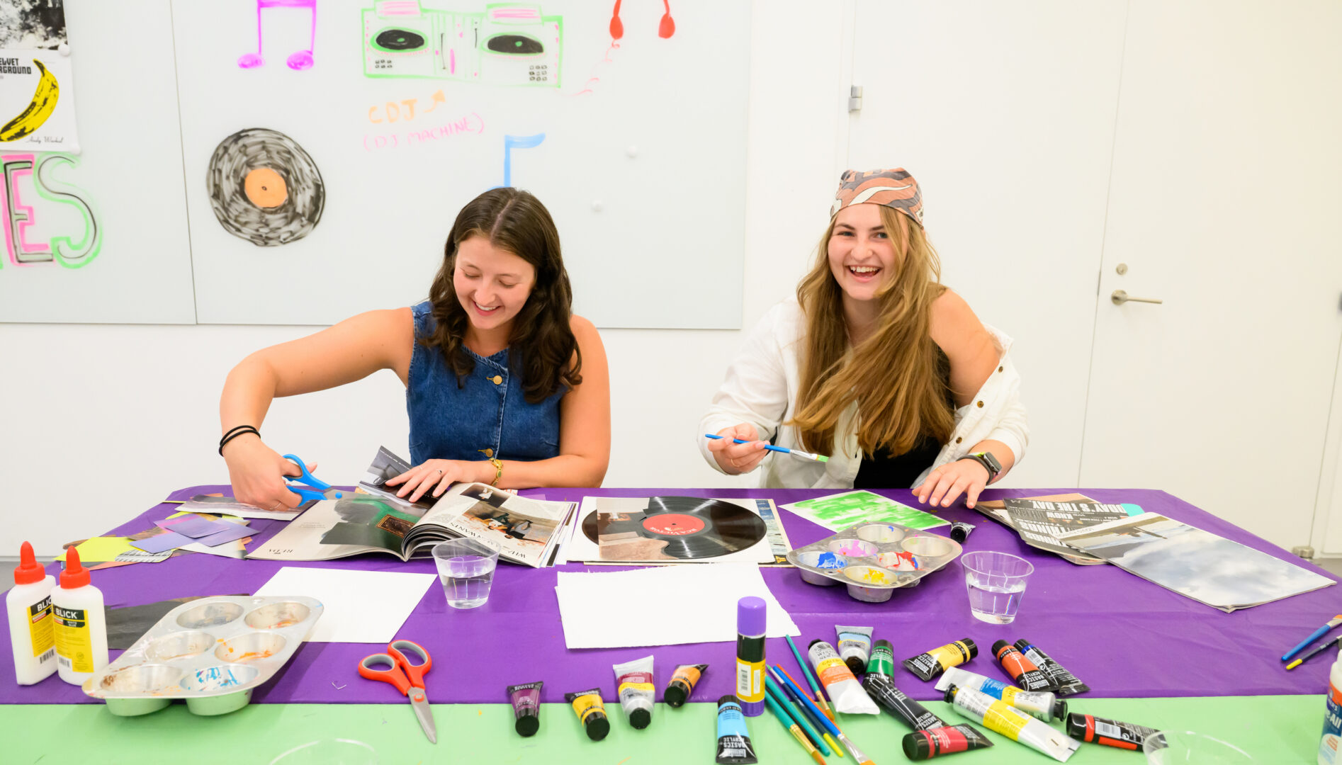 Two people laughing and making collage art at a table full of craft supplies.