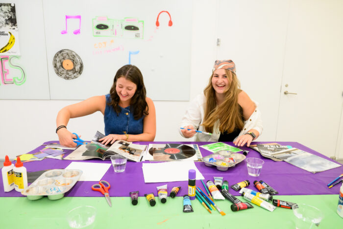Two people laughing and making collage art at a table full of craft supplies.